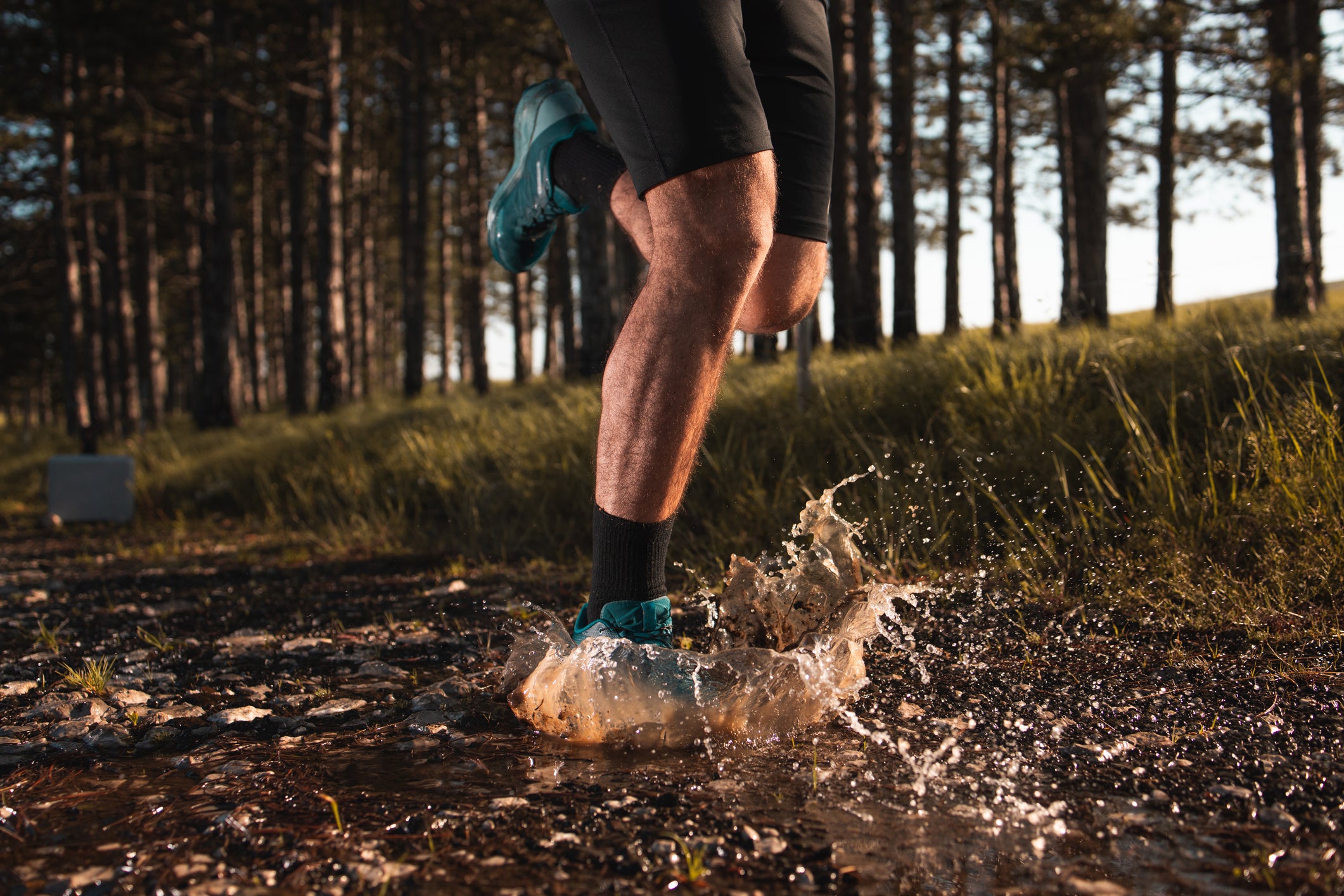 Shot of the legs of a man who is stepping into a puddle while running through the forest.