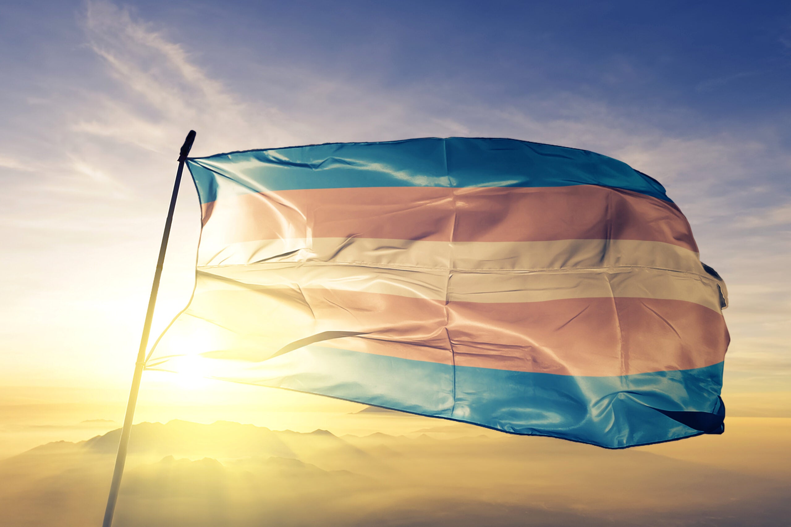 Transgender Pride flag on flagpole textile cloth fabric waving on the top sunrise mist fog
