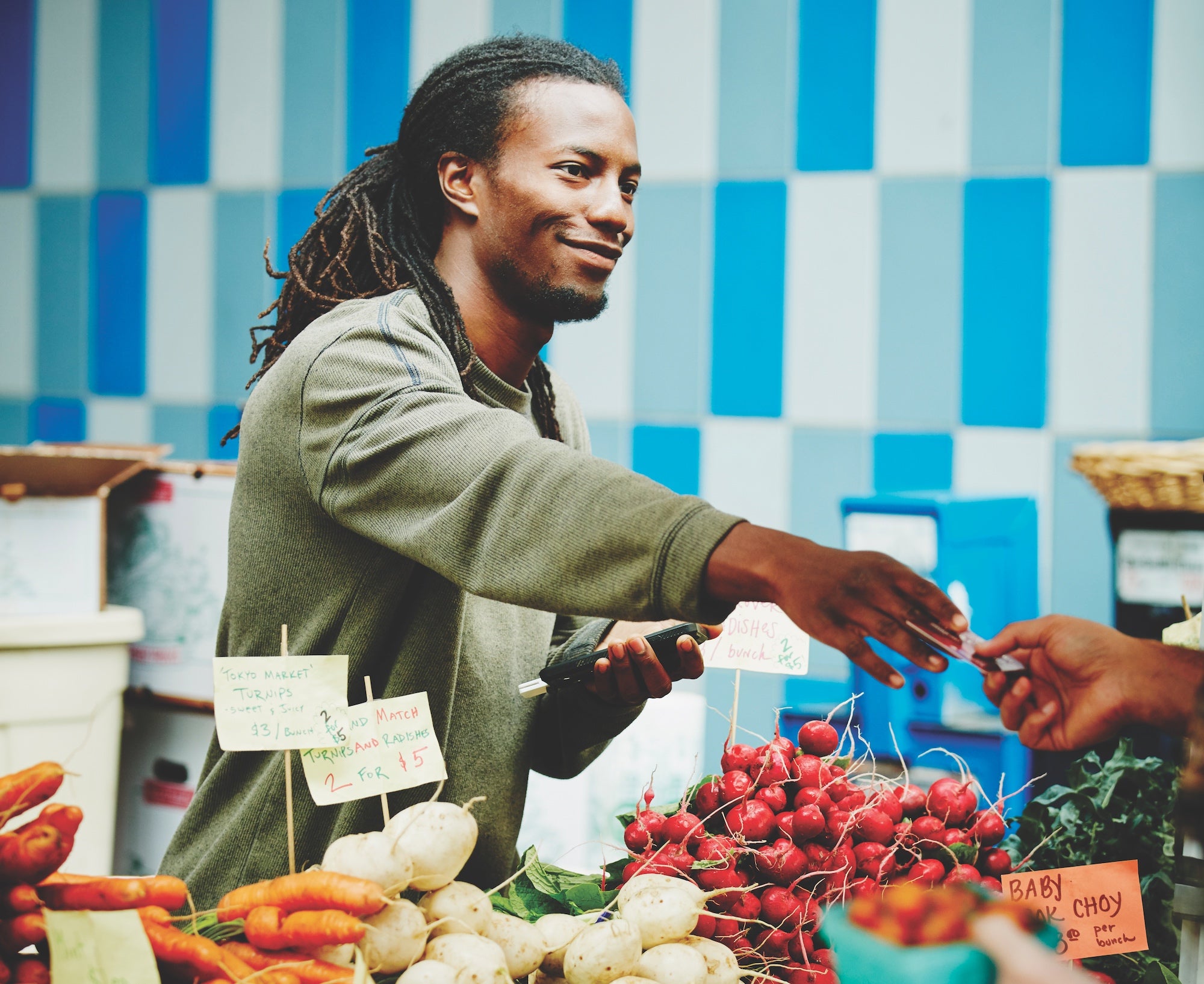 Smiling organic farmer taking customer credit card to run transaction with smartphone at farmers market