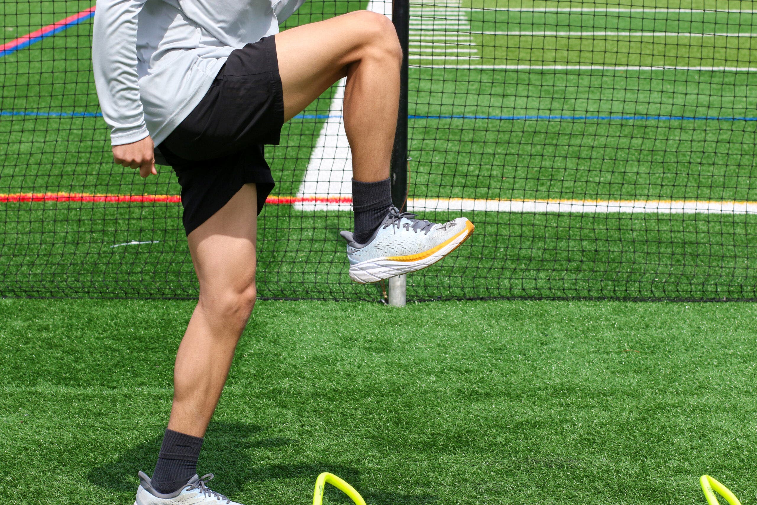 Athlete standing over small yellow hurdles on a green turf field