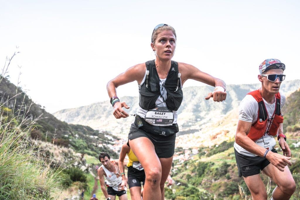 Female runner in a black vest runs up a mountain.