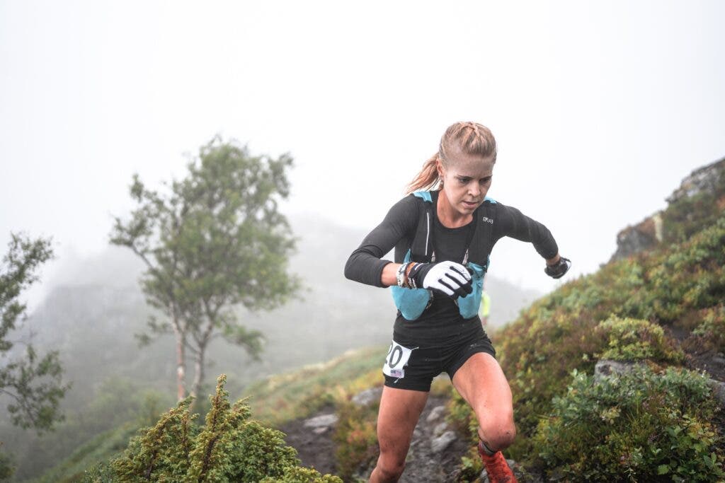 A runner in blue hydration vest and gloves runs up a mountain.