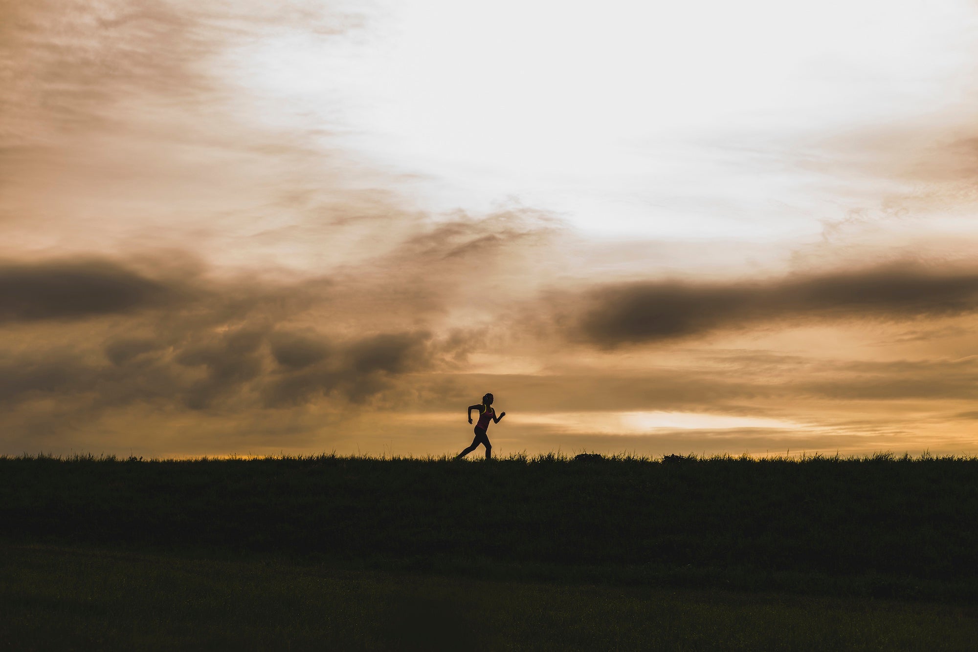 The silhouette of a solo woman runs at dusk