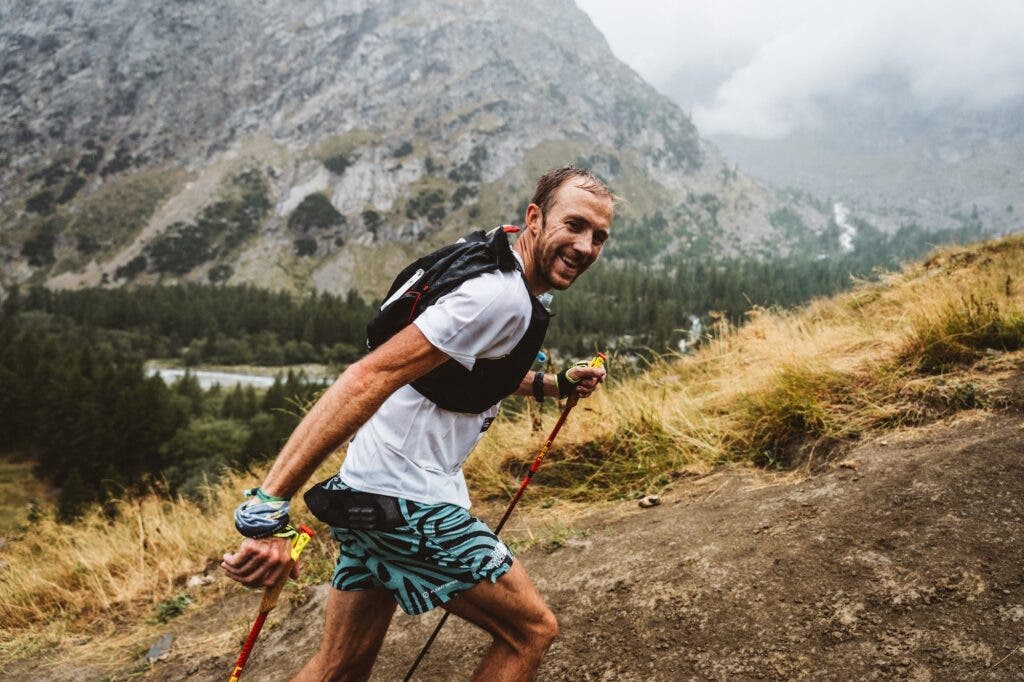 A man in a white shirt is hiking up a hill