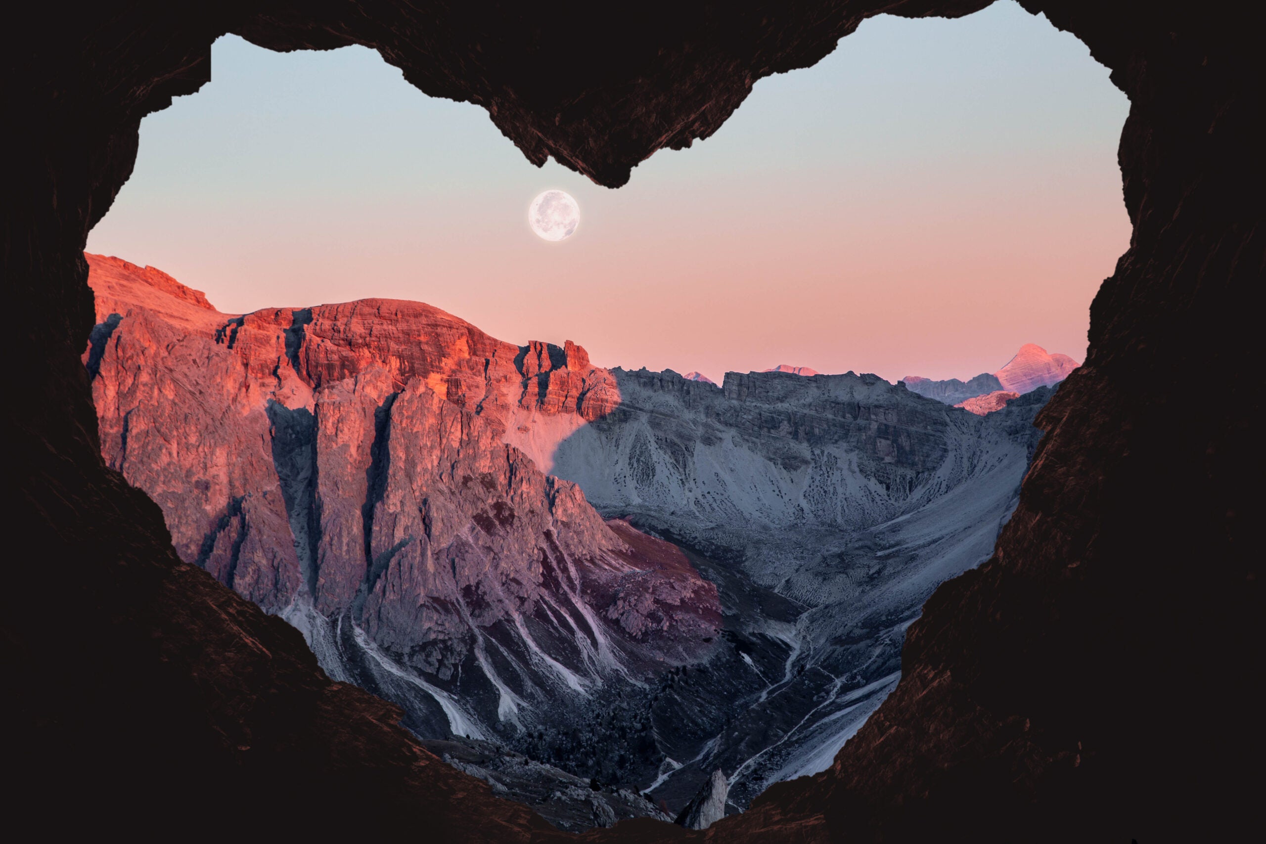 Composition of the Alps mountains during sunset with full moon from a cave with heart shape.