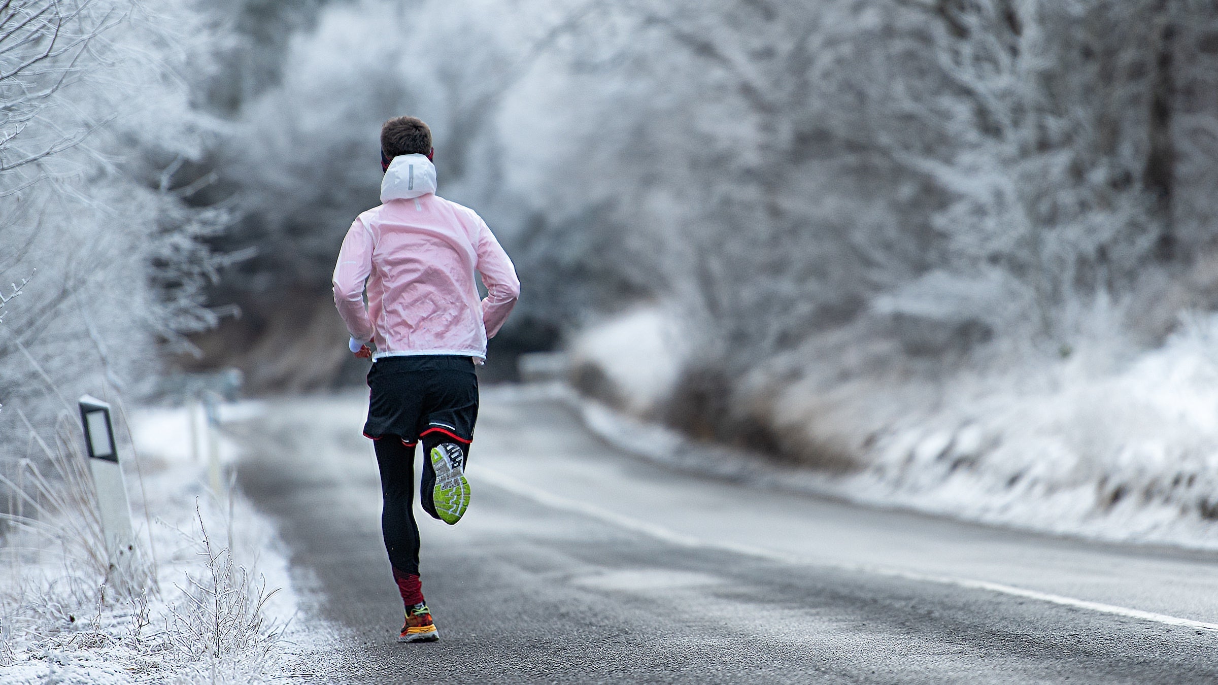 a man with a light red/pink jacket runs down a snowy road.