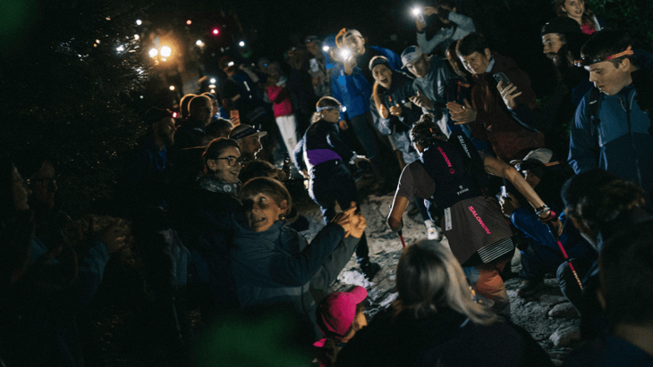 Photo of Courtney Dauwalter ascending a climb in the night through a tunnel of people illuminated by headlamps and phone flashes.