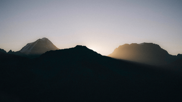 Photo of alpine peaks silhouetted by a rising sun.