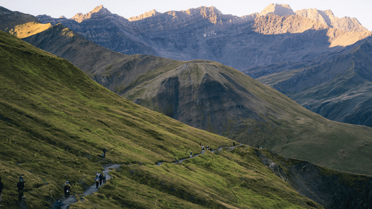 Photo of a string of hikers making their way along a traversing trail through an alpine landscape.