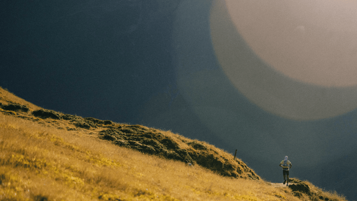 Photo of Chris Myers descending to La Fouly through an open, green alpine meadow at dawn.