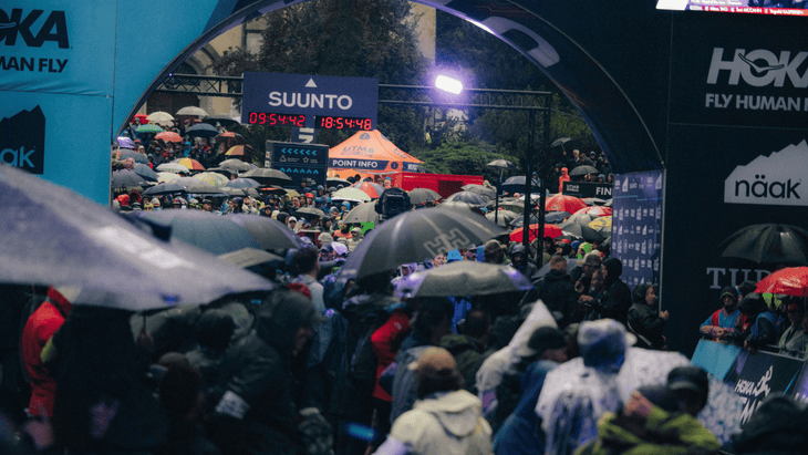 Photo of umbrellas dominating the crowd at the UTMB start line with banners and archways showing advertisements in the background.